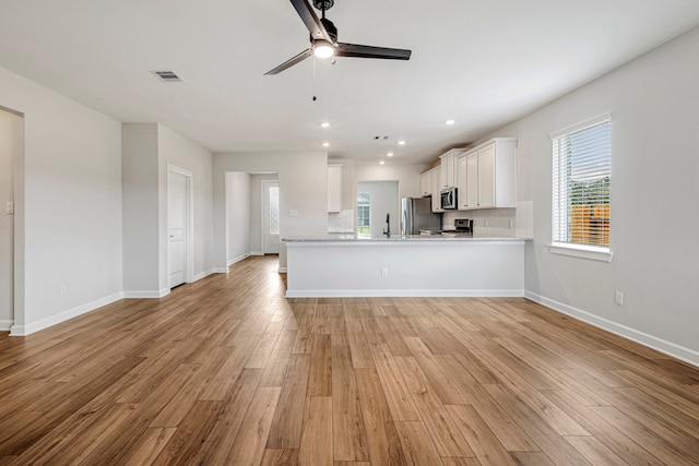 kitchen with light hardwood / wood-style flooring, appliances with stainless steel finishes, white cabinetry, backsplash, and kitchen peninsula