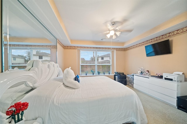 bedroom featuring ceiling fan, a tray ceiling, and carpet