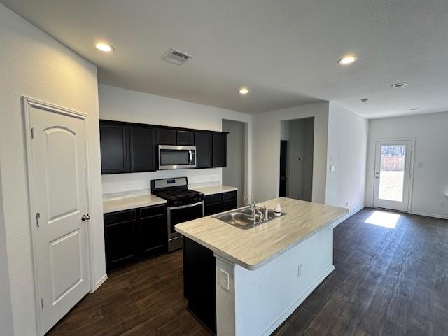 kitchen with appliances with stainless steel finishes, a kitchen island with sink, sink, and dark hardwood / wood-style flooring