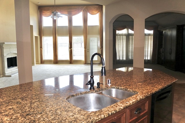 kitchen featuring decorative light fixtures, dishwasher, sink, dark stone counters, and a high ceiling