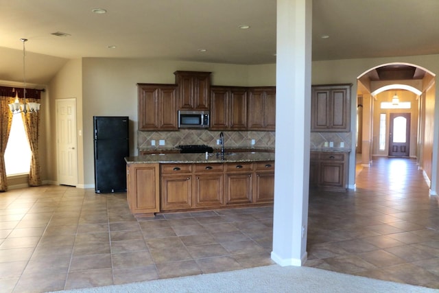 kitchen featuring black refrigerator, dark stone countertops, a notable chandelier, and decorative backsplash