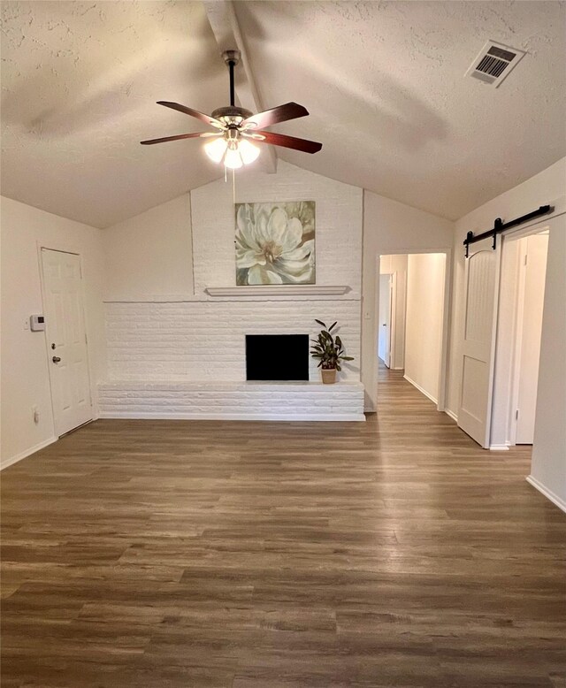 unfurnished living room with dark wood-type flooring, ceiling fan, lofted ceiling with beams, a textured ceiling, and a barn door