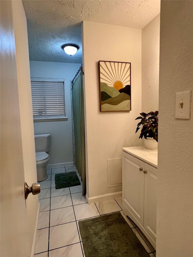 bathroom with tile patterned flooring, vanity, a textured ceiling, and toilet