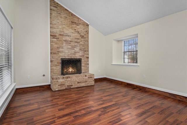 unfurnished living room featuring lofted ceiling, a brick fireplace, dark hardwood / wood-style flooring, and a textured ceiling