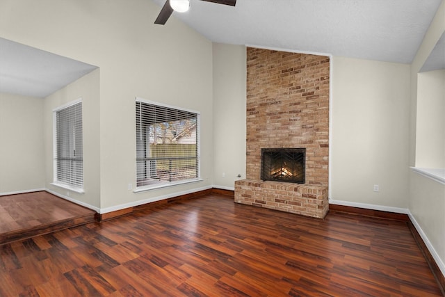 unfurnished living room featuring dark wood-type flooring, ceiling fan, a brick fireplace, and a textured ceiling