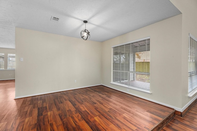 unfurnished dining area with a textured ceiling, dark wood-type flooring, and a healthy amount of sunlight