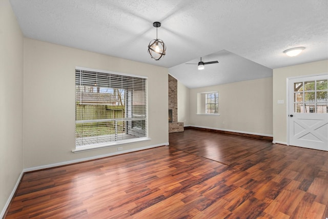 unfurnished living room featuring dark hardwood / wood-style floors, lofted ceiling, ceiling fan, a brick fireplace, and a textured ceiling