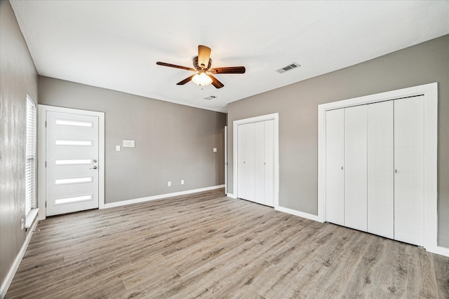 unfurnished bedroom featuring multiple closets, ceiling fan, and light hardwood / wood-style flooring