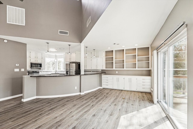 kitchen featuring white cabinetry, kitchen peninsula, pendant lighting, stainless steel appliances, and light hardwood / wood-style floors
