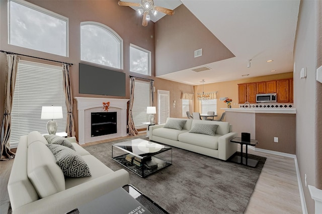 living room featuring light hardwood / wood-style floors, ceiling fan, and a high ceiling