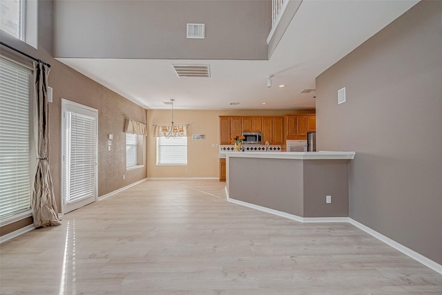 kitchen with stainless steel appliances, light hardwood / wood-style floors, decorative light fixtures, kitchen peninsula, and a chandelier