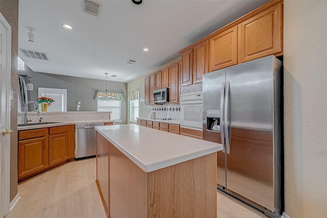 kitchen featuring sink, appliances with stainless steel finishes, a kitchen island, decorative light fixtures, and light wood-type flooring