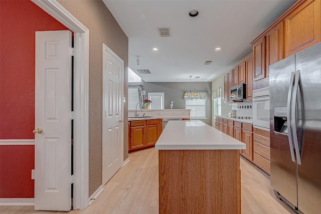 kitchen featuring sink, light hardwood / wood-style flooring, appliances with stainless steel finishes, a kitchen island, and decorative light fixtures