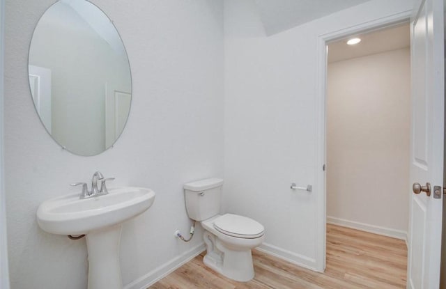 half bath with toilet, baseboards, and wood finished floors