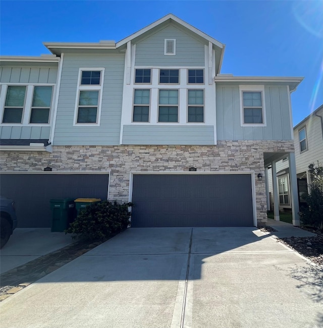 view of front facade featuring a garage, driveway, board and batten siding, and stone siding