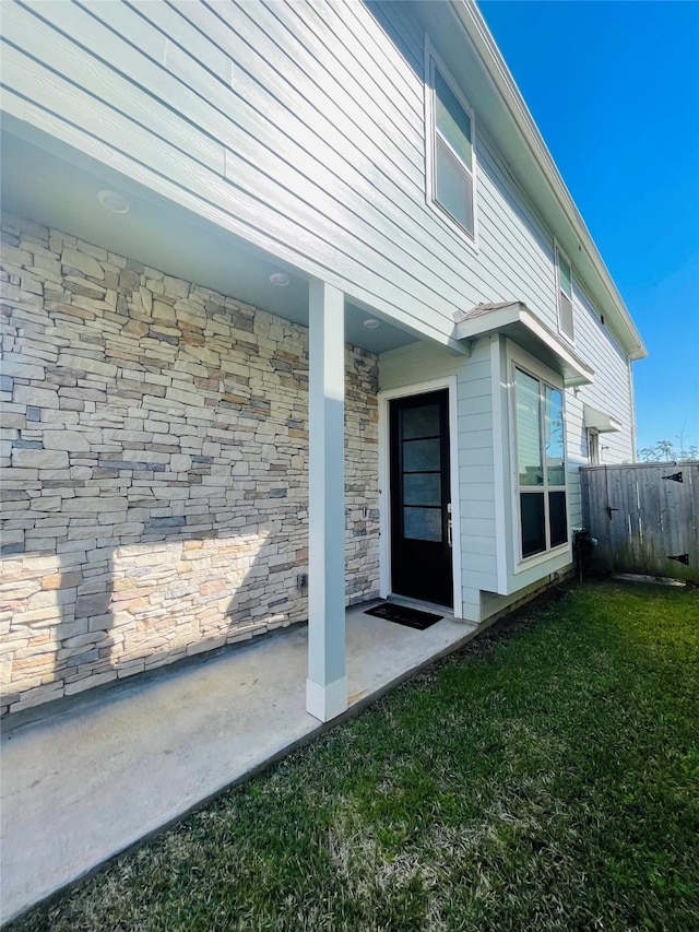 view of home's exterior featuring stone siding, a yard, and fence