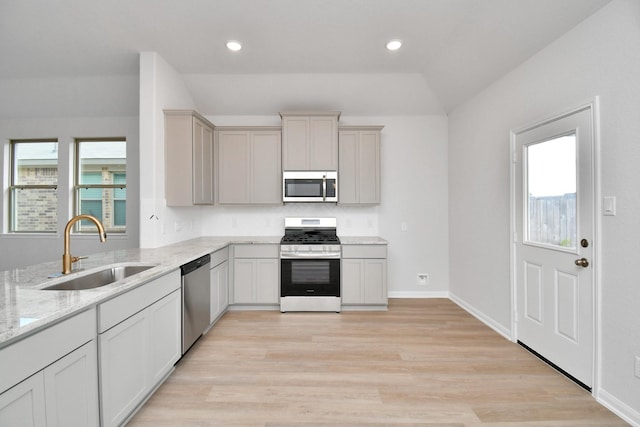 kitchen with stainless steel appliances, a healthy amount of sunlight, light stone countertops, and sink