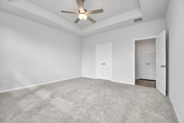 unfurnished bedroom featuring a closet, carpet flooring, ceiling fan, and a tray ceiling