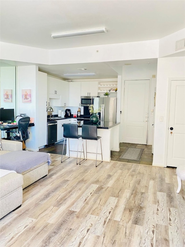 kitchen with appliances with stainless steel finishes, a breakfast bar, white cabinetry, a center island, and light wood-type flooring