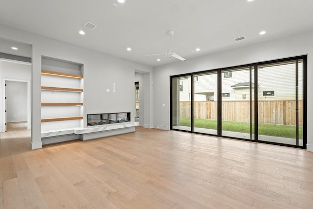 unfurnished living room with built in shelves, ceiling fan, and light hardwood / wood-style flooring