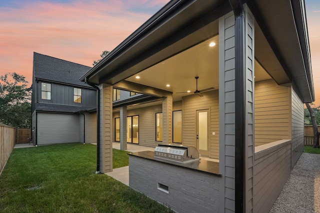 property exterior at dusk with exterior kitchen, a lawn, ceiling fan, and a patio area