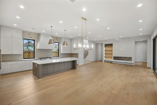 kitchen featuring premium range hood, a spacious island, white cabinets, decorative light fixtures, and light wood-type flooring