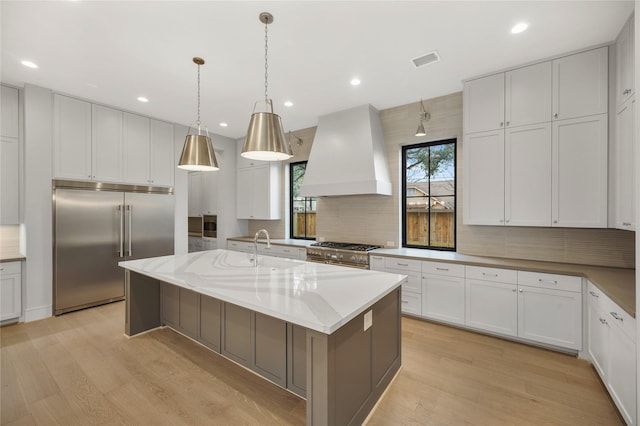 kitchen featuring custom exhaust hood, high end appliances, a kitchen island with sink, and white cabinetry