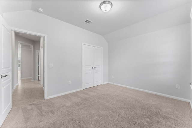 unfurnished bedroom featuring lofted ceiling, light carpet, and a closet