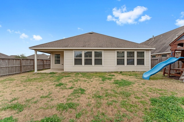 back of house featuring a lawn and a playground