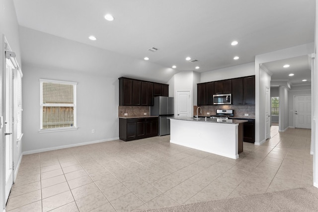 kitchen featuring light tile patterned floors, appliances with stainless steel finishes, a kitchen island with sink, dark brown cabinets, and decorative backsplash