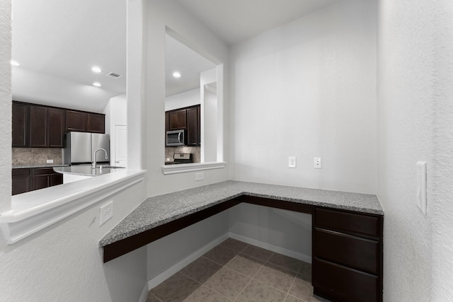 kitchen featuring dark brown cabinetry, light stone counters, light tile patterned floors, appliances with stainless steel finishes, and decorative backsplash