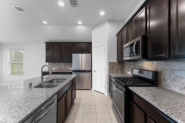 kitchen featuring light tile patterned flooring, dark brown cabinetry, sink, stainless steel appliances, and light stone countertops