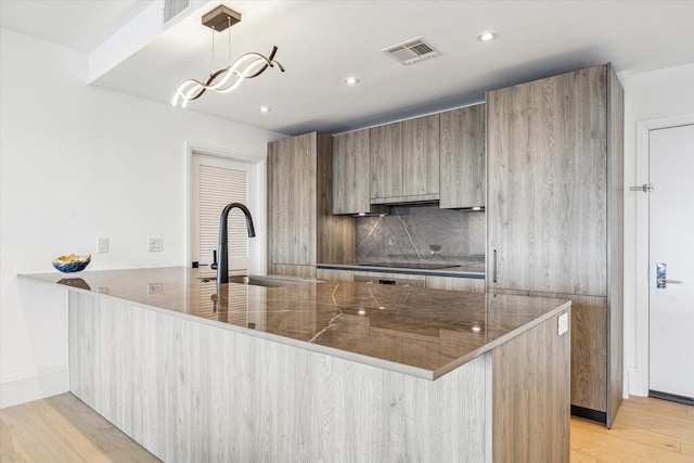 kitchen with black electric cooktop, kitchen peninsula, hanging light fixtures, and light hardwood / wood-style flooring