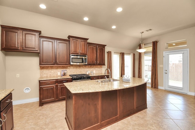 kitchen with appliances with stainless steel finishes, an island with sink, sink, backsplash, and light stone countertops