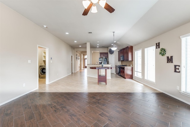 kitchen with washer / dryer, a breakfast bar area, hanging light fixtures, a center island with sink, and appliances with stainless steel finishes