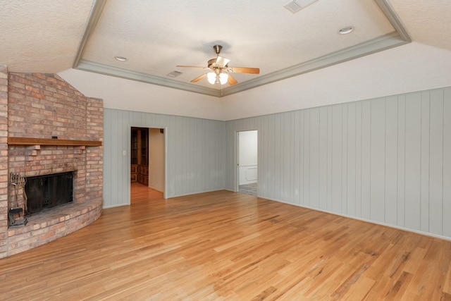 unfurnished living room with a brick fireplace, a tray ceiling, ceiling fan, and light wood-type flooring