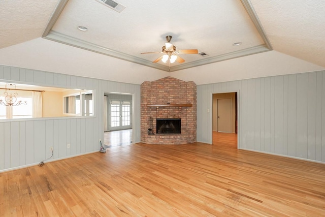 unfurnished living room featuring lofted ceiling, ceiling fan with notable chandelier, light hardwood / wood-style floors, and a raised ceiling