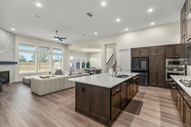 kitchen featuring a fireplace, sink, a kitchen island with sink, dark brown cabinetry, and stainless steel appliances