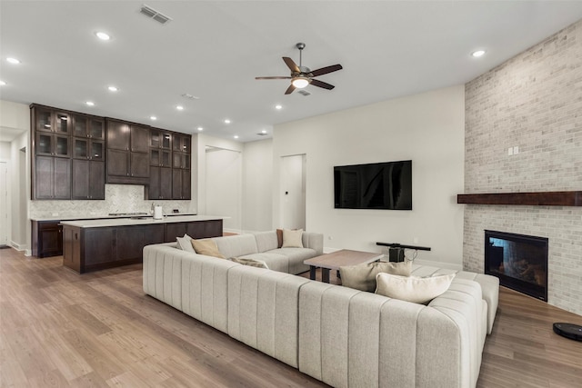 living room featuring ceiling fan, a brick fireplace, and light wood-type flooring