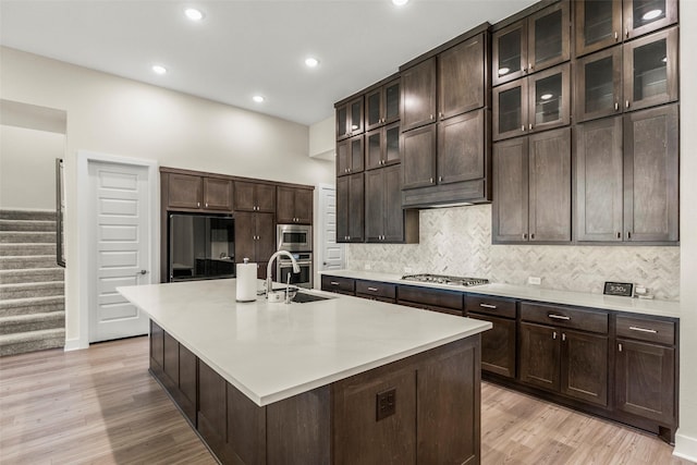 kitchen with appliances with stainless steel finishes, sink, decorative backsplash, a kitchen island with sink, and light hardwood / wood-style flooring