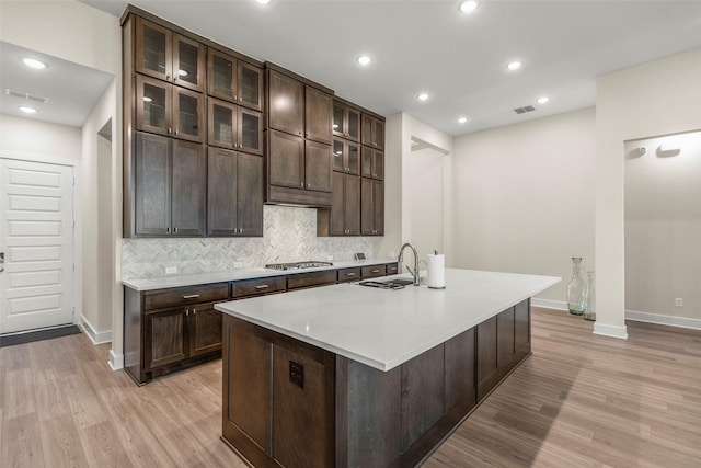 kitchen featuring dark brown cabinets, stainless steel gas stovetop, sink, and a center island with sink