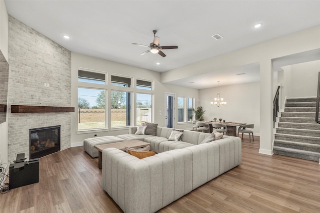 living room featuring ceiling fan with notable chandelier, a fireplace, and light wood-type flooring