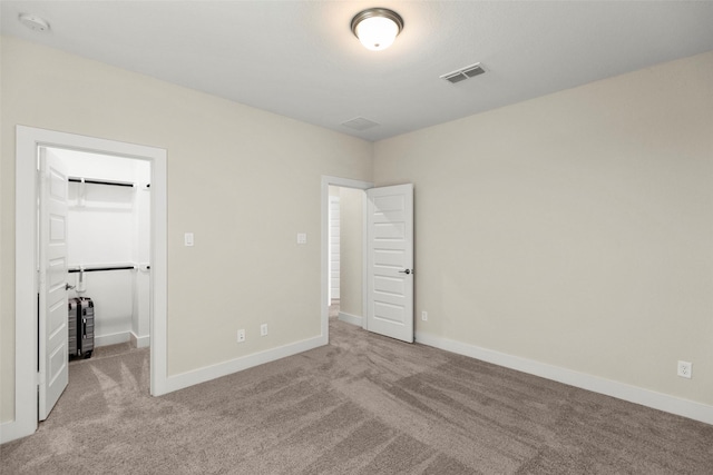 unfurnished bedroom with a walk in closet, light colored carpet, and a closet