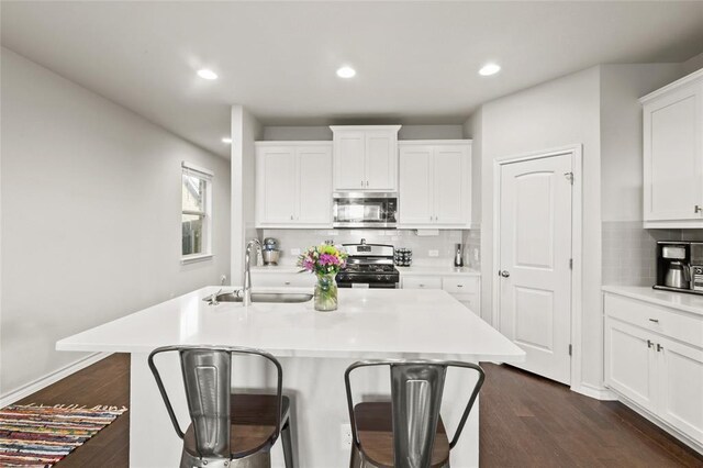 kitchen with dark wood-type flooring, a breakfast bar area, white cabinetry, stainless steel appliances, and a kitchen island with sink