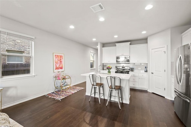 kitchen with a wealth of natural light, appliances with stainless steel finishes, a center island with sink, and white cabinets