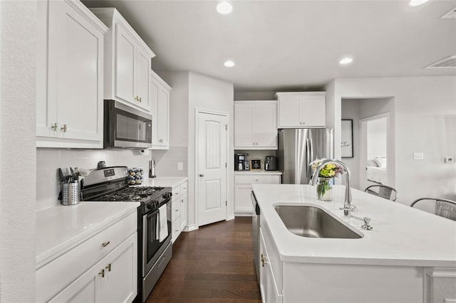 kitchen with appliances with stainless steel finishes, dark hardwood / wood-style floors, sink, white cabinets, and a center island with sink