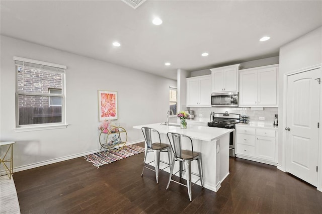 kitchen with a breakfast bar, appliances with stainless steel finishes, white cabinetry, a center island with sink, and decorative backsplash