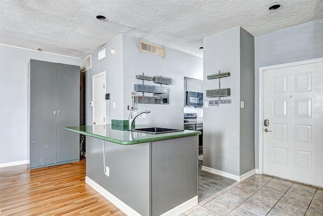 kitchen with light wood-type flooring, sink, a textured ceiling, and electric range