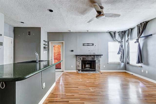 unfurnished living room with a fireplace, sink, ceiling fan, light hardwood / wood-style floors, and a textured ceiling