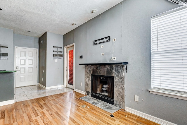 unfurnished living room featuring a tiled fireplace, a textured ceiling, and light hardwood / wood-style flooring